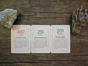 Three oracle cards displayed on a wooden surface with two crystals beside them, showing the messages 487 Imagine, 251 Listen, and 201 Patterns, symbolizing creativity, intuition, and mindful awareness.